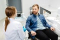 Blonde female dentist in dental office talking with male patient and preparing for treatment. Handsome bearded man in dentist Royalty Free Stock Photo