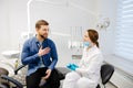 Blonde female dentist in dental office talking with male patient and preparing for treatment. Handsome bearded man in dentist Royalty Free Stock Photo