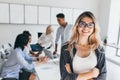 Blonde female executive posing with smile and arms crossed during brainstorm with managers. Indoor portrait of european