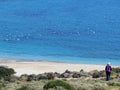 Blonde female hiker approaching beautiful sandy beach and blue and turquoise sea with seagulls Greece