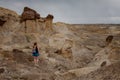 Blonde female hiker walks among rock hoodoos in an arid desert landscape in the Bisti Badlands, De-Na-Zin Wilderness, San Juan Cou