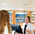 Blonde female pharmacist advises young woman customer at the counter of a pharmacy