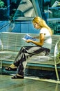 A Blonde female sitting reading a magazine