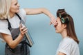 Blonde female stylist spraying client`s brown hair on rollers over blue Royalty Free Stock Photo