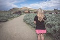 A blonde female walks on a path toward more abandoned buildings in the ghost town of Bodie California