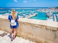Blonde girl admires the harbour of Otranto, Apulia, Italy.