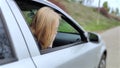 The blonde girl became ill from driving a car. Vomiting forced her to look out of the car so that the vomit would not enter the pa