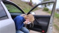 The blonde girl became ill from driving a car. Vomiting forced her to look out of the car so that the vomit would not enter the pa