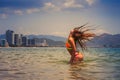 blonde girl in bikini stands in sea shaken head lifts hair up