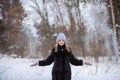 blonde girl in a black fur coat and a blue hat against the backdrop of a winter snowy forest. She throws snow and it flies in the Royalty Free Stock Photo