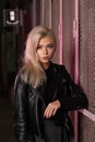 blonde girl in a black leather jacket posing on a dark background and pink lattice, rock style Royalty Free Stock Photo