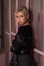 blonde girl in a black leather jacket posing on a dark background and pink lattice, rock style Royalty Free Stock Photo