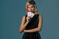 Blonde girl in black stylish dress showing two playing cards, posing against blue background. Gambling entertainment Royalty Free Stock Photo