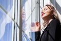 A blonde girl in a black suit stands near the window and enjoys the sunlight Royalty Free Stock Photo