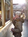 Blonde girl with blond hair paints her lips with lipstick near the window