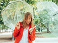 .blonde girl with blue eyes and dressed in red gabardine balances with two transparent umbrellas in a park in Madrid, Spain