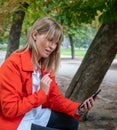 Blonde girl with blue eyes and dressed in red gabardine talks on the phone going up to a bench in a park