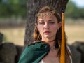 Blonde girl with elf ears poses in the field with a bow and a green cape