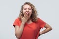 Blonde girl bored and yawning tired covering mouth with hand. Studio shot, white background. Restless and sleepiness