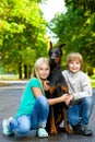 Blonde girl and boy hugs beloved dog or doberman