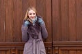 Blonde girl in a brown coat with fur, high boots posing on a background of an old wooden door Royalty Free Stock Photo