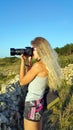 Blonde girl with a camera with a large lens shooting outdoor
