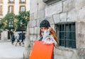 Blonde girl with coat and bonnet, carries two shopping bags while smiling at the camera while walking through a city Royalty Free Stock Photo