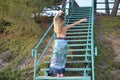 Blonde girl dances on stairs back to the camera and raises and move apart her arms