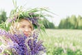 A blonde girl in a flower lupine wreath with a bouquet of lupines gently smiles and inhales the fragrance of flowers in