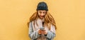 Blonde girl with hat, coat and scarf looks at her mobile phone smiling Royalty Free Stock Photo