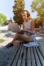 A blonde girl with headphones sitting on a bench on a sunny day, using a laptop. Royalty Free Stock Photo