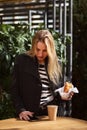 Blonde girl holding a Paper Cup of coffee and muffin sitting in a cafe. Royalty Free Stock Photo