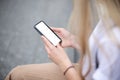 blonde girl holding a phone with a blank screen in her hands while sitting on the street. place for your design