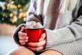 A blonde girl holding a red cup of hot chocolate with marshmallows on Christmas tree lights bokeh background Royalty Free Stock Photo