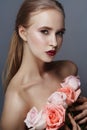 Blonde girl holding rose flowers near her face. Beauty portrait of a woman on a dark background. Perfect makeup, beautiful body Royalty Free Stock Photo