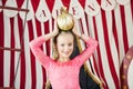 Blonde girl holds golden ball on her head on circus decorations background. World circus day