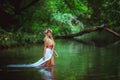 Blonde girl knee deep in water in summer green forest