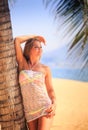 blonde girl in lace closeup leans on palm trunk on beach