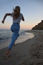 A blonde girl in jeans and a T-shirt is running along the shore of the evening sea. Back view Royalty Free Stock Photo