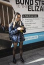 Blonde girl with long hair in a short skirt and a leather jacket looks at the phone on the street corner