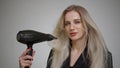 Blonde girl with long straight hair dries her hair with a hair dryer