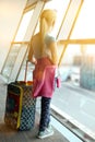 Blonde girl with luggage is standing near window at the airport