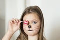 Blonde girl with a make-up imitating a cat holds in her hand a chupa chups.