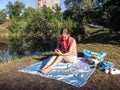 Blonde girl with pigtails sits near the lake with a laptop. A woman in casual clothes uses gadgets while relaxing outdoors on a Royalty Free Stock Photo