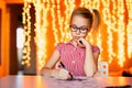 Blonde girl in the pink dress and big black glasses drawing santa claus. Christmas and New Year theme, yellow bokeh