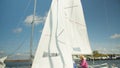 Blonde girl in pink jacket sitting on the stern of a yacht, white sail and yacht blue sky background. Slow motion