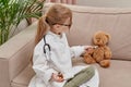 A blonde girl plays the profession of a doctor and feeds a toy to a teddy bear. Royalty Free Stock Photo