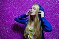 Blonde girl in a purple hoodie listening to music in blue headphones on pink background. hipster teenager enjoys listening to the Royalty Free Stock Photo