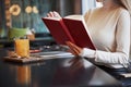 Blonde girl read a book with red cover in the restaurant with table and yellow drink on it Royalty Free Stock Photo