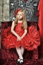 Blonde girl in a red elegant dress with a red hairpin in her hair sitting on an armchair Royalty Free Stock Photo